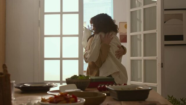 Woman giving her female friend flowers and hugging her during dinner paty at modern apartment