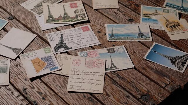 A collection of vintage postcards is spread out on a rustic wooden table. The postcards showcase famous landmarks of Paris, capturing scenes of the Eiffel Tower and other attractions.