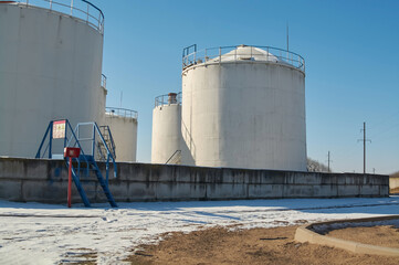 White storage fuel tanks in oil industrial refinery plant area against blue clear sky background, low angle view with copy space