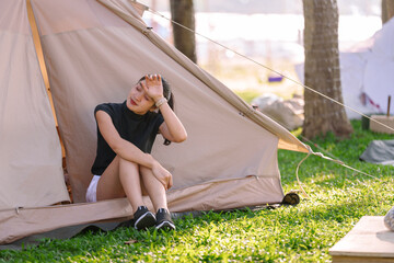 Young woman sitting at the entrance of her tent, feeling the heat during a summer camping trip,...