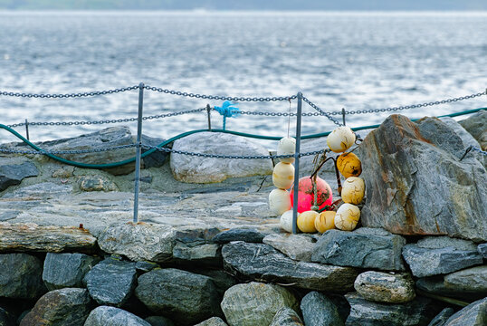 Colorful buoys and chains rest on a rocky pier with gentle waves lapping against the shore during soft morning light.