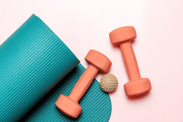 Teal yoga mat is partially rolled up, next to two coral dumbbells and a beige massage ball. Perfect for health and fitness concepts