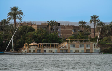 Large luxury traditional Egyptian dahabeya river cruise boat moored on the Nile bank with buildings in background