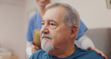Fototapeta premium Nurse, support and elderly man with brush for hair care, assistance and helping hand at home. Professional caregiver, happy and person with conversation for healthcare, help and grooming service