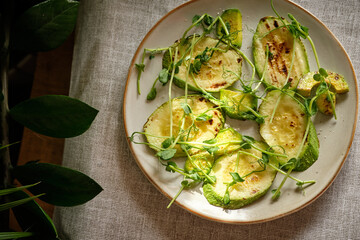 Fried zucchini and pea sprouts on a white plate, top view. White background.
