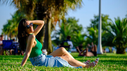 A young brunette woman enjoying the sun on a sunny day, stretched out and sunbathing in a grassy...