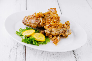 Crispy fried chicken legs lying on white plate with vegetable garnish