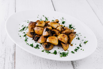 Fried mushrooms with dill lying on white plate on white table