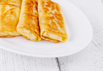 Thin pancakes with filling lying on white plate on wooden table