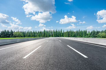 Asphalt road and green forest under blue sky with clouds