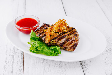 Grilled steak with crispy onions and sauce on white plate