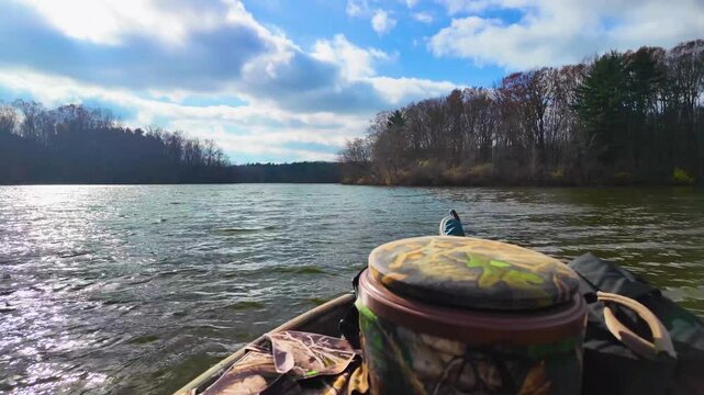 A POV from a boat trolling over rippled water, bucket in sight, under a bright sky with clouds.