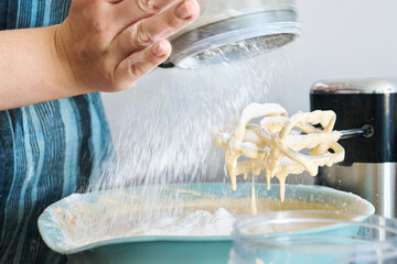 Cook in an apron sifts flour into bowl to make cake on kitchen counter surrounded by kitchen utensils and blender