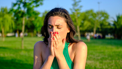 Close-up of a young brunette woman sneezing while sick in a scenic park