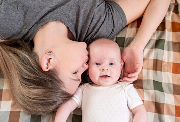 Mom kisses her baby while lying on a cozy blanket in a warm and nurturing environment