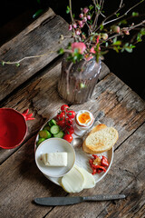 Bowl with boiled egg, cherry tomatoes, toast, butter, cheese, cucumber and hot pepper.