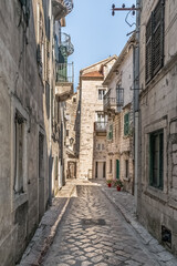 Peaceful, sunlit alleyway in the historic town of Kotor, Montenegro. Traditional stone buildings with charming balconies and colorful flower pots, reflecting the quaint atmosphere of Kotor Old Town