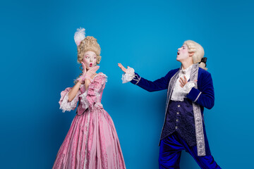 Elegant couple in baroque outfits poses against a vibrant blue background, capturing the charm of...