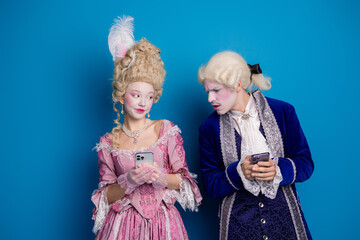 Elegantly dressed couple in historical costumes engages with modern smartphones against a vibrant...