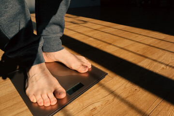 Man measuring her weight using scales on floor on a sunny morning. Man checking his weight on weight scale.