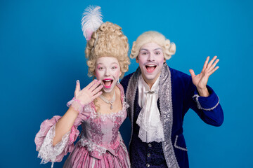 Joyful couple in elegant baroque costumes against a blue background embracing the fun of a historic...