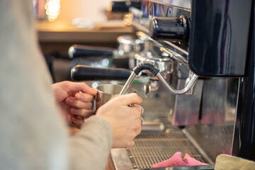 Barista steaming milk with coffee machine. Female barista making coffee in cafe.
