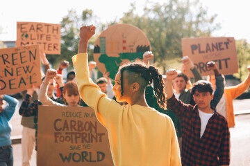 Young activists protesting for climate change action - Group of diverse young activists at a climate protest holding signs and raising fists in support of environmental causes