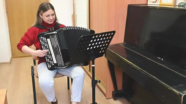 A woman in a red sweater plays the bayan in a classroom, focusing on her learning progress. Learning finger coordination and melody, she embraces music as a path to self-improvement and creativity