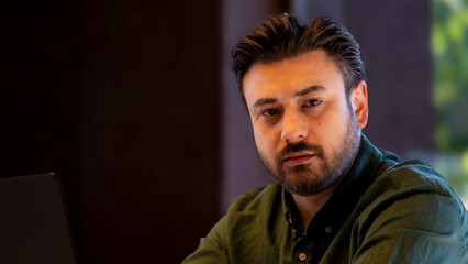 Obraz premium An attractive, slightly overweight middle-aged businessman working with his laptop at a café outside of the office, posing for the camera