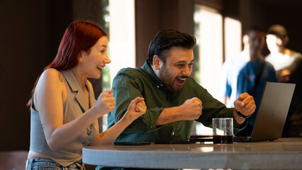 Middle-aged businessman and young businesswoman celebrating enthusiastically during a meeting with...