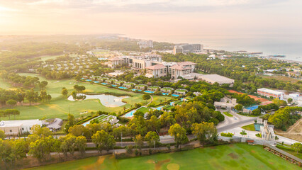 Aerial panoramic view of a luxury seaside resort with golf courses, private villas, and pools at sunrise