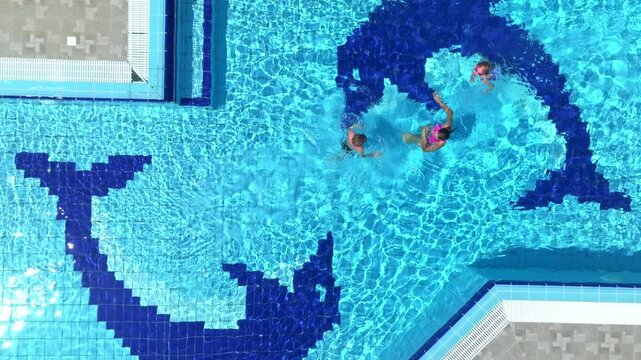 Top down drone shot above a Mother and kids swimming in a pool in sunny Greece