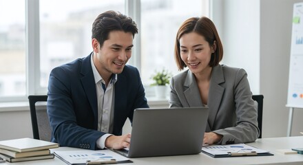 Fototapeta premium Two businesspeople, a man and a woman, smiling while working together on a laptop, reviewing data and charts on a desk in a modern office; concept for business collaboration, teamwork, and partnership