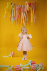 A little girl in a pink dress with balloons on a yellow background