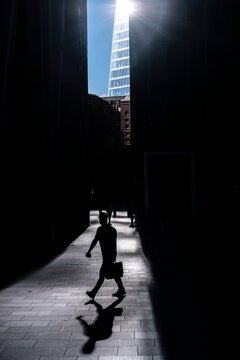 Silhouettes of people walking in a sunlit alley with The Shard in the background.