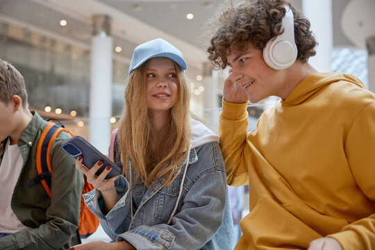 Teen boy sharing favorite music track in headphones to girl friend