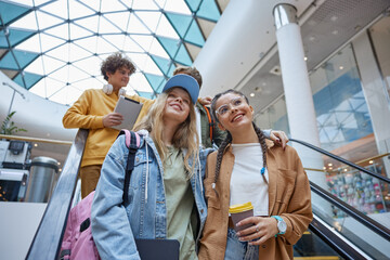 Happy carefree teenagers group riding escalator in shopping mall
