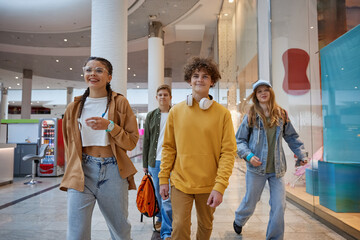 Happy overjoyed teenagers fooling around running through shopping mall corridor