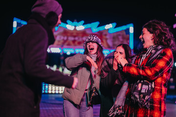 A group of friends shares a joyful moment at an illuminated carnival at night, expressing happiness and connection. Their laughter and energy contribute to a bright and festive atmosphere.