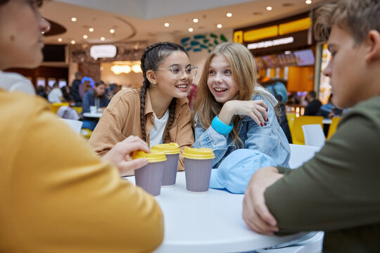 Teenage friends having fun while eating and drinking at food court of shopping mall