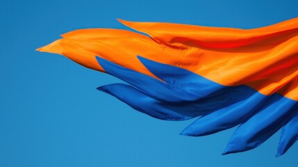 Fototapeta premium Bright Orange and Blue Flag Waving Against Clear Blue Sky