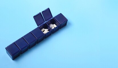 Weekly pill organizer in dark blue color with white tablets inside sitting against a light blue background