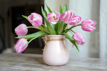 Delicate pink tulip flowers in a pink vase on the window in the spring morning. White spring interior