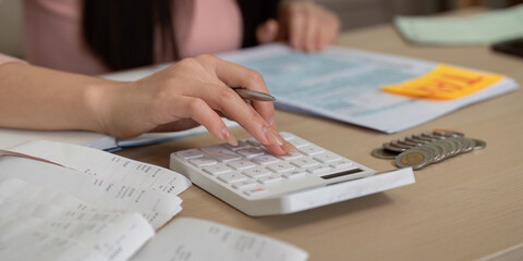 Woman using calculator for tax planning and financial analysis, surrounded by paperwork.