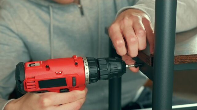 Man customizing furniture, reshape table or fix wardrobe, using screwdriver. Craftsman hands refurbishing domestic spaces. Performing servicing or mechanical adjustments