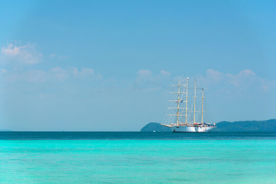 A white sailboat is anchored in the ocean, amidst a bright sky, bright sunshine and the turquoise sea in front of Koh Kradan, Trang, Thailand. Summer outdoor nature holiday serenity, copy space. 