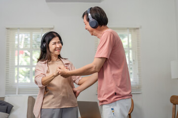 Fototapeta premium Diverse older couple dancing at home with wireless headphones, enjoying music together.