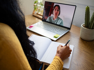 Hand of an Hispanic woman taking notes in a notebook while conversing at an online coaching...