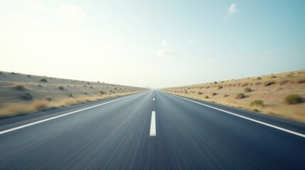 Fototapeta premium Asphalt ribbon unwinding towards a distant horizon, under a pale sky, flanked by sun-baked terrain and sparse vegetation.