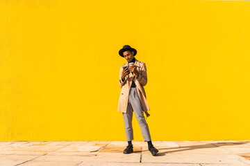 Young man with hat, using smartphone, drinking coffee